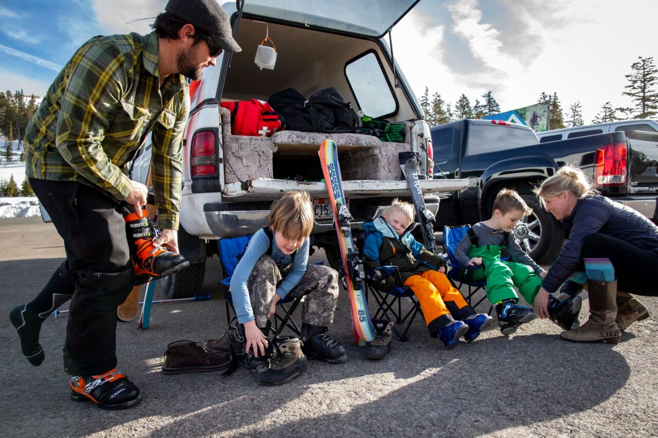 family sitting outside the car, putting ski boots on